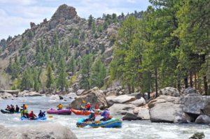 Several rafters move down the gorgeous river in Buena Vista, Colorado with mountains and trees in the background