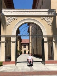 A girl in a wheelchair smiling under a big arch at the University of Southern California