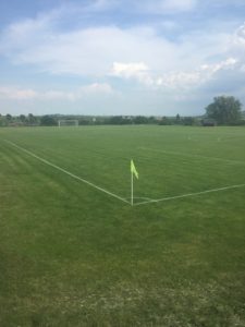 This photo shows one of the fields we played on while abroad. It has a very bright green field with a beautiful blue sky in the background. 