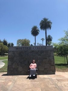 A girl posing in front of a sign that reads "Whittier College."